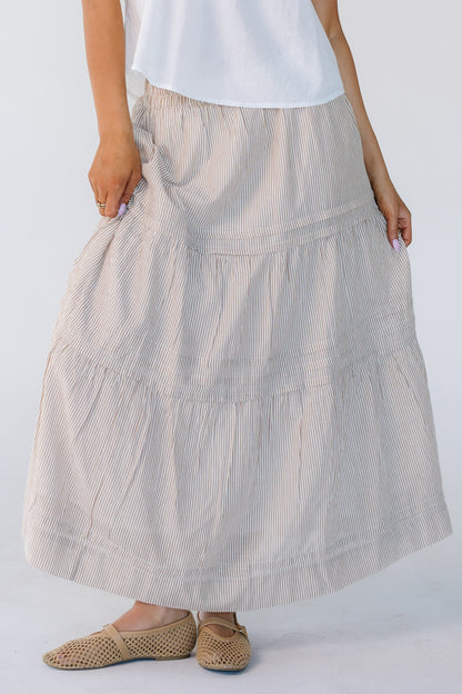 Woman wearing a camel vertical stripe skirt with horizontal pleats and 2 gathered tiers.
