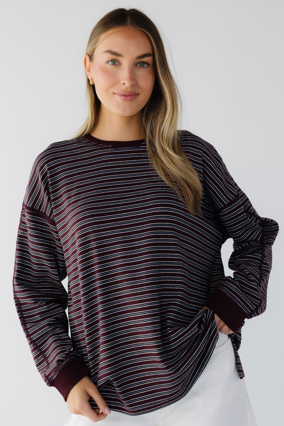 A young woman wearing an oversized burgundy stripe long sleeve tee with exposed seam details.