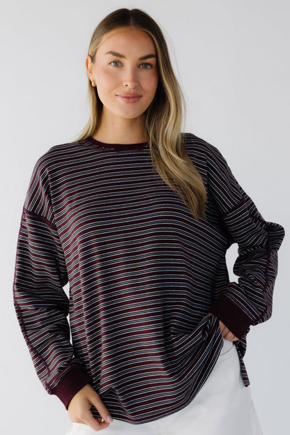 A young woman wearing an oversized burgundy stripe long sleeve tee with exposed seam details.