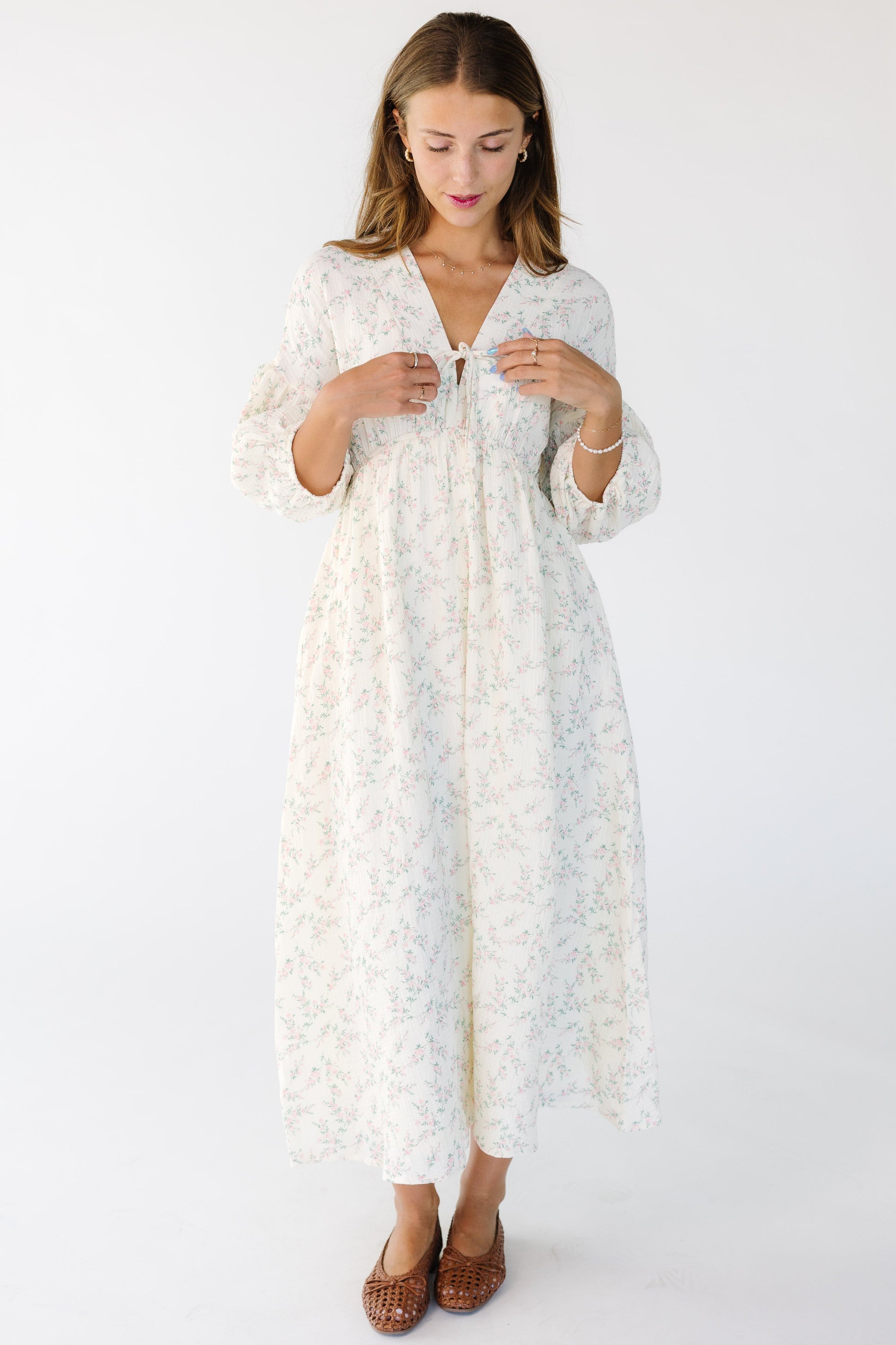 Woman wearing a cream and pink floral midi dress with a bow on the V-neckline with half length sleeves.