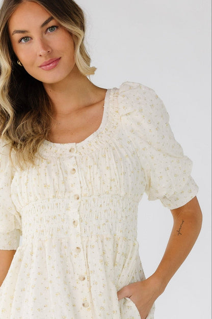 Close view of a woman wearing a button down midi dress with a scoop neckline, wide elastic waist and large puff sleeves. And side pockets.