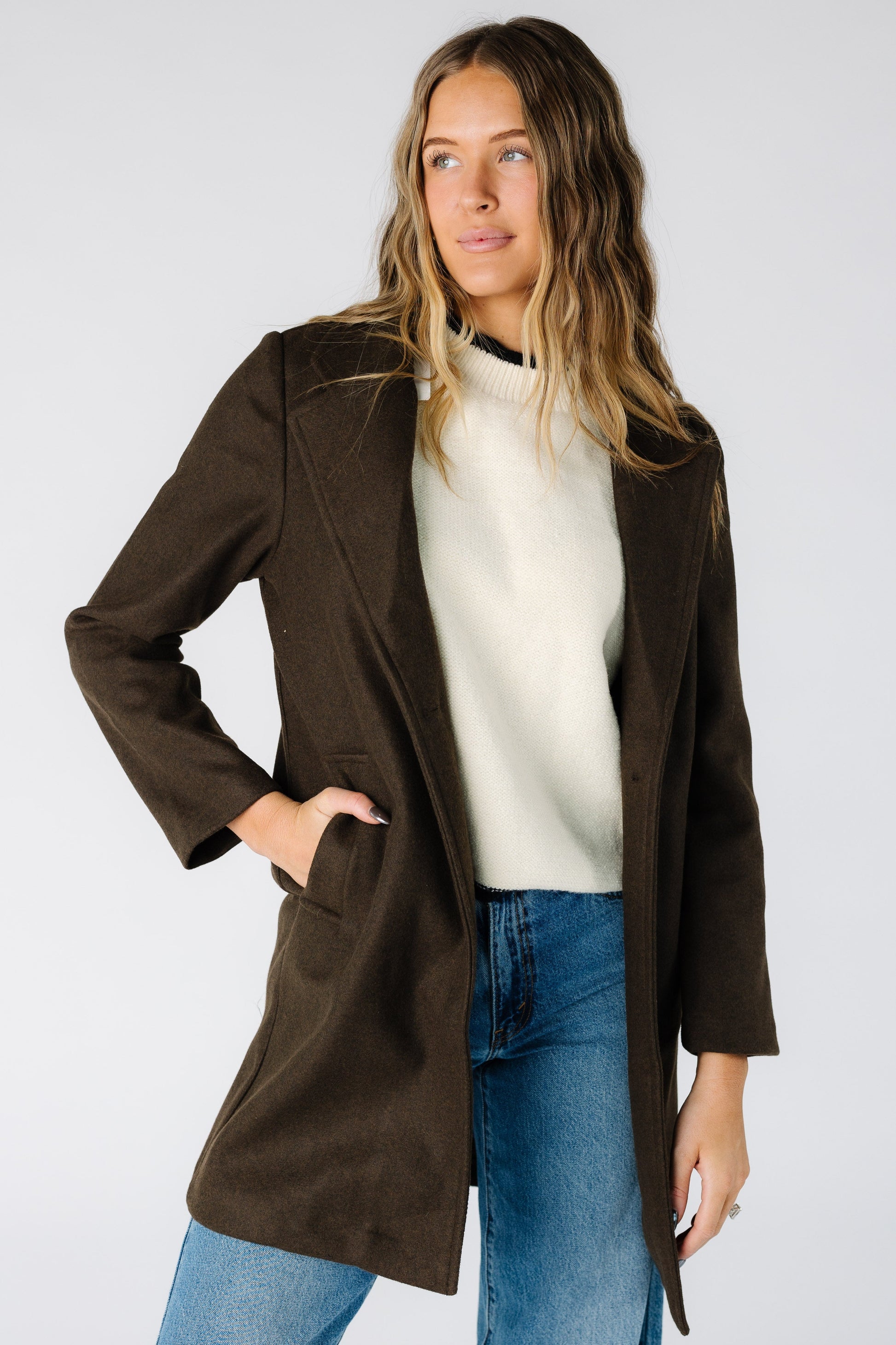 Woman wearing a dark brown jacket with a mid thigh length and long sleeves