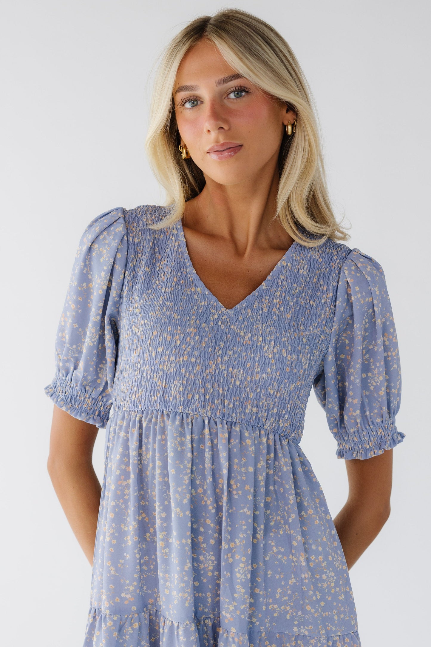 Young woman wearing a modest light purple floral dress with a smocked bodice, short puff sleeves and a V-neckline.
