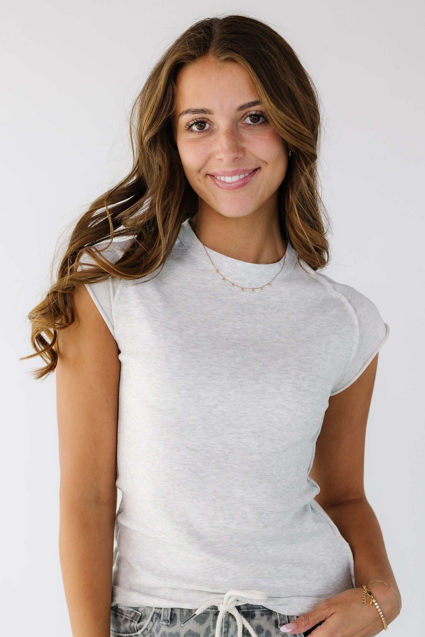 Woman wearing a light grey close fitting rib knit top with short sleeve made of a smooth fabric and with rolled hems.