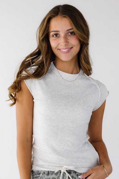 Woman wearing a light grey close fitting rib knit top with short sleeve made of a smooth fabric and with rolled hems.