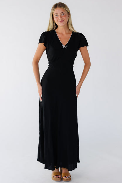 Young woman wearing an elegant black maxi dress with a white trimmed V-neckline, short flutter sleeves and a flare skirt.