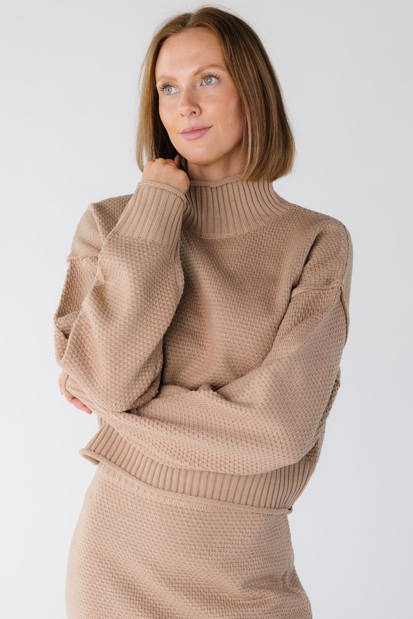 Close view of a woman wearing a long sleeve textured sweater with a ribbed turtleneck