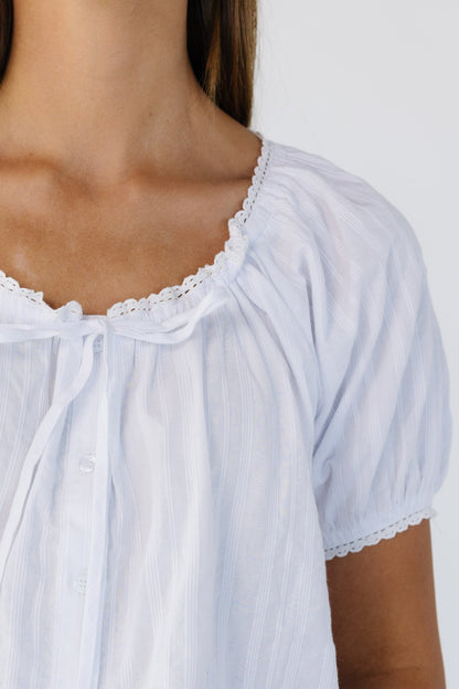 Close view of a young woman wearing a white button down, loose fitting blouse with a tie.
