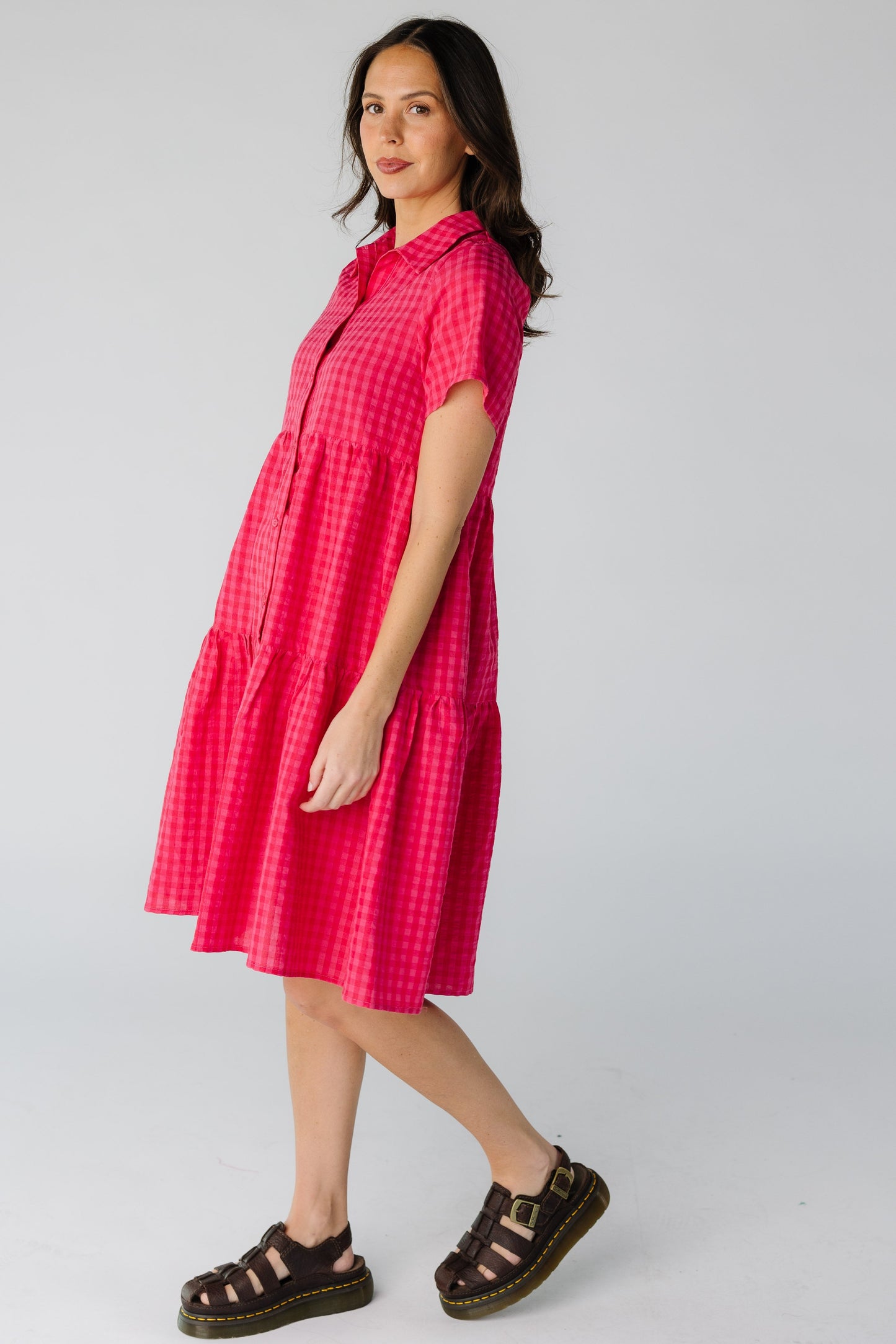 Side view of a woman wearing a knee length dress in red and pink gingham with short sleeves.