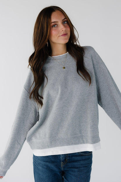 Young woman wearing a grey oversized sweatshirt with a faux white tee crew neckline and hem.