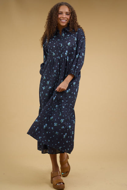 Young woman wearing a modest blue floral midi dress with a button down bodice, pointed collar and long sleeves.