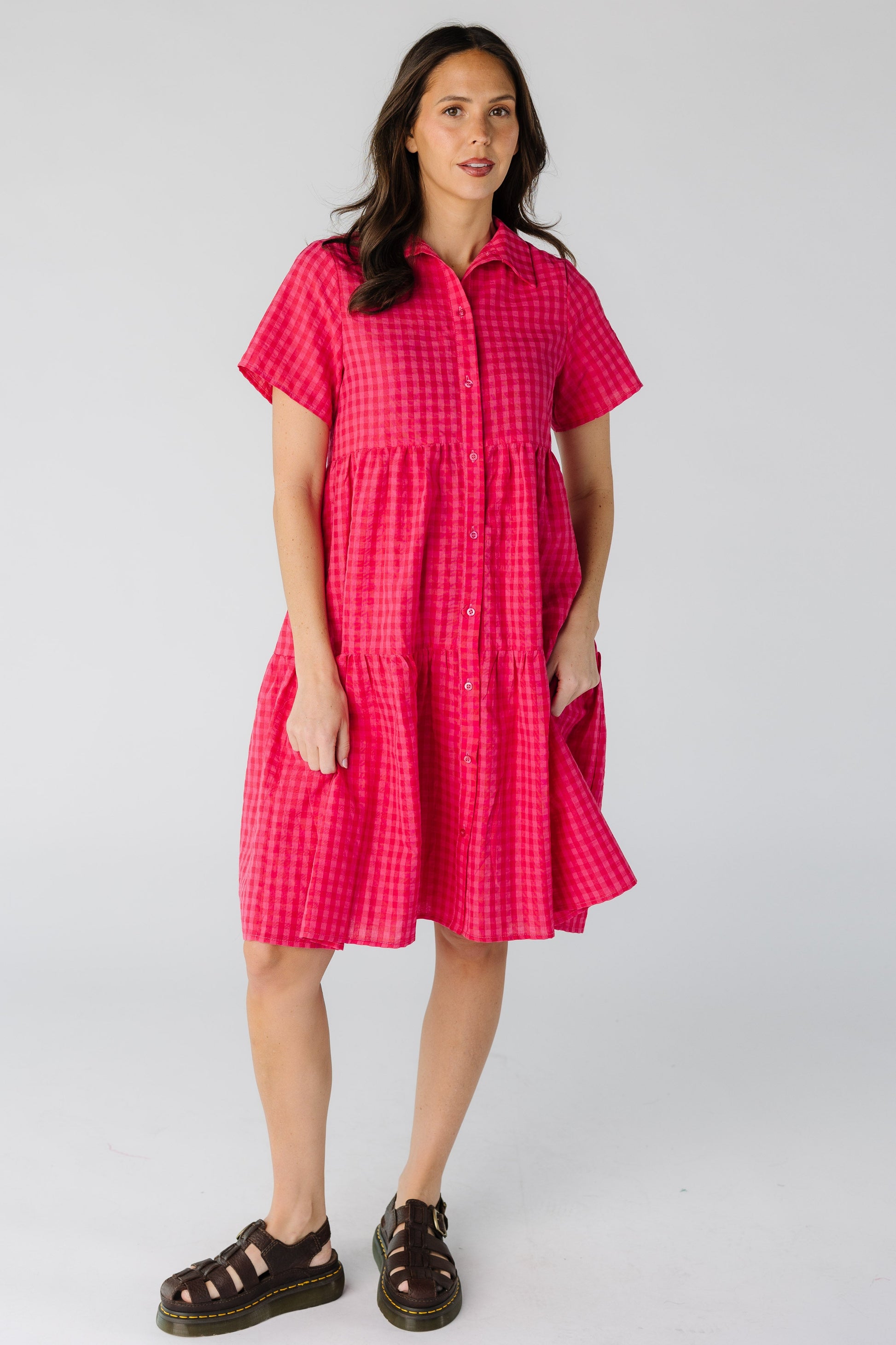 Woman wearing a modest red and pink gingham button down dress with short sleeves and a pointed collar.