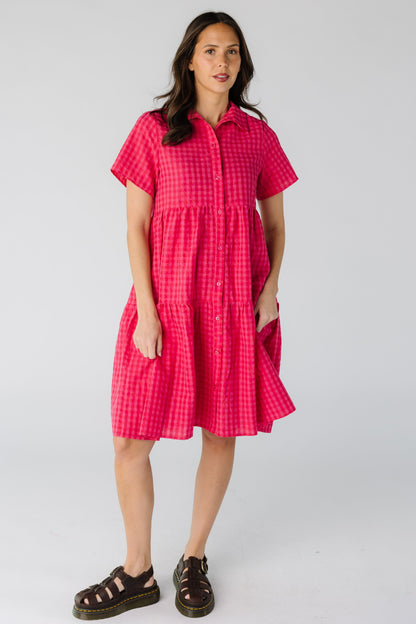 Woman wearing a modest red and pink gingham button down dress with short sleeves and a pointed collar.