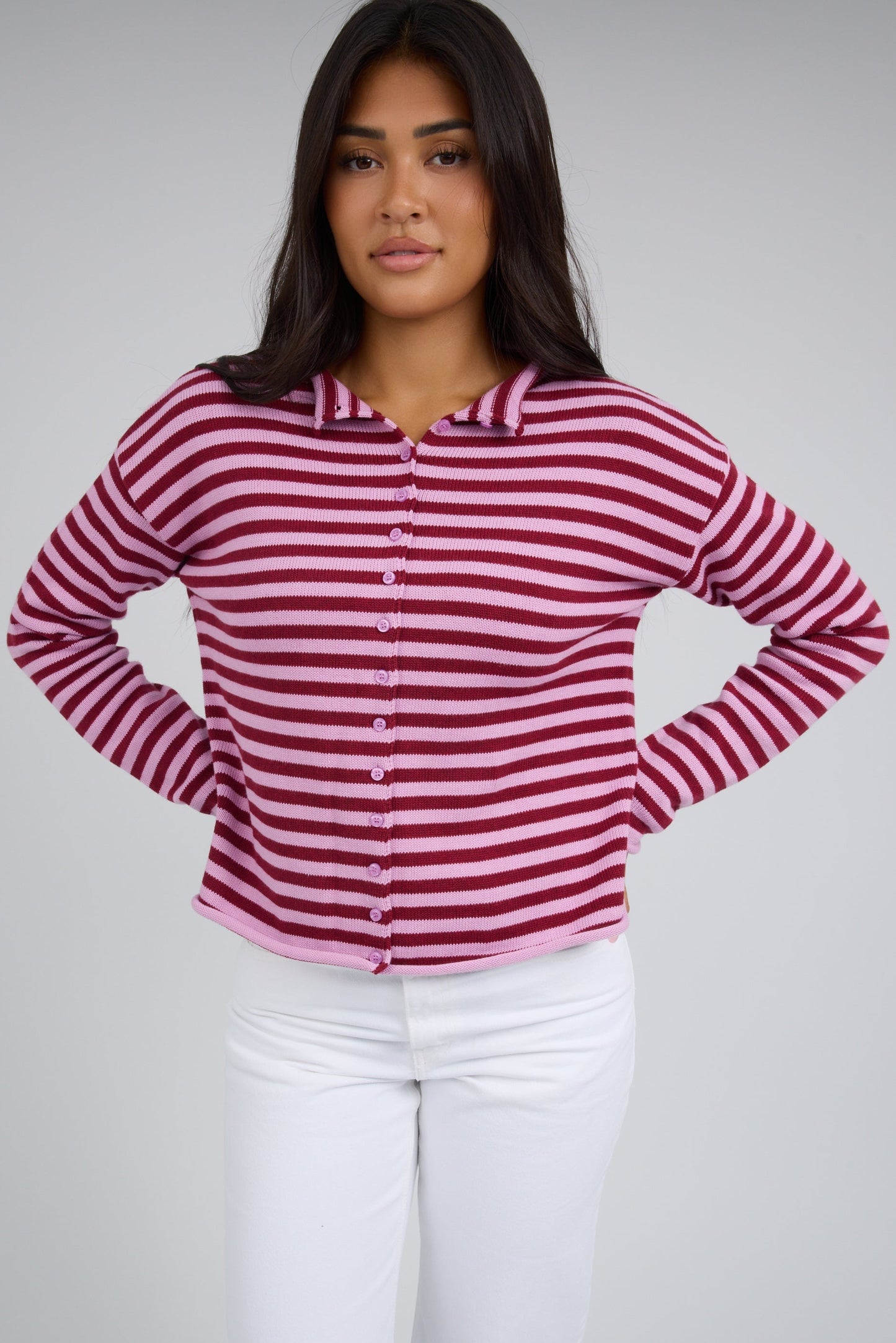 Woman wearing a pink & red stripe button down cardigan with rolled hems and long sleeves.