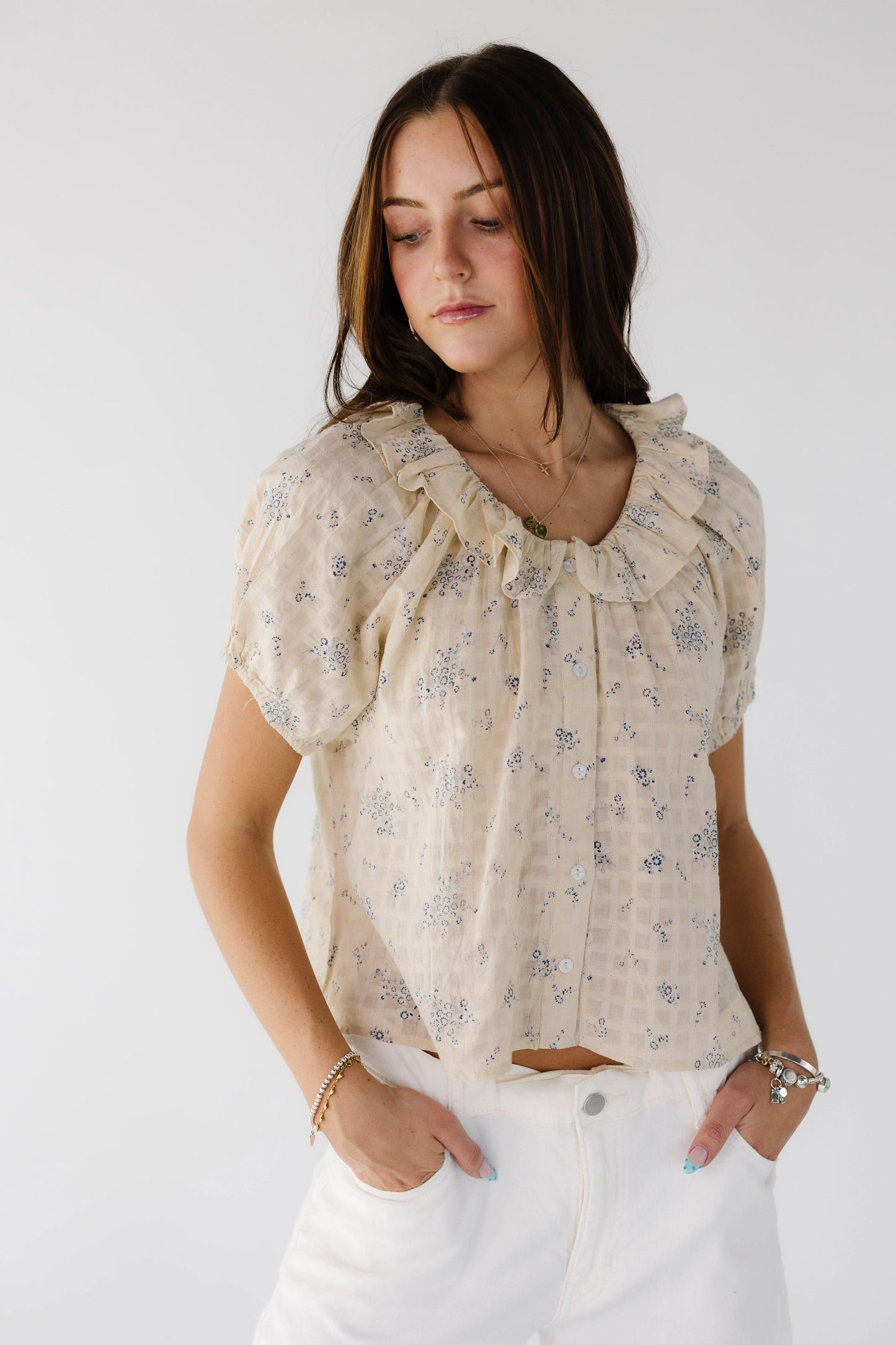 Young woman wearing a modest beige & blue floral button down top with short sleeves and a ruffle collar.