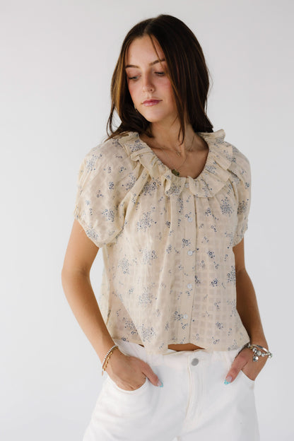 Young woman wearing a modest beige & blue floral button down top with short sleeves and a ruffle collar.