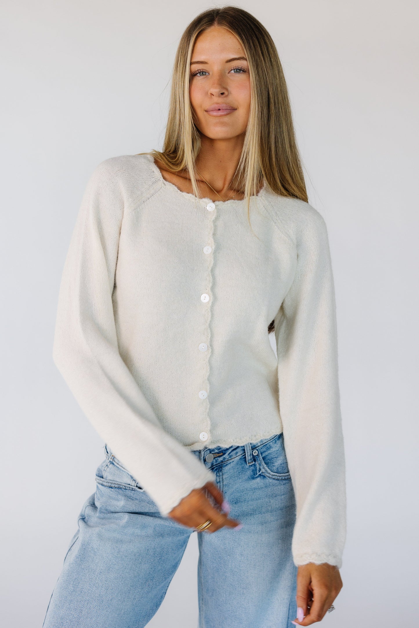 Woman wearing a modest cream cardigan with scallop edge, round neckline and long sleeves with scallop cuffs.