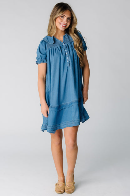 Woman wearing a denim loose dress with short sleeves and smocked yoke. 