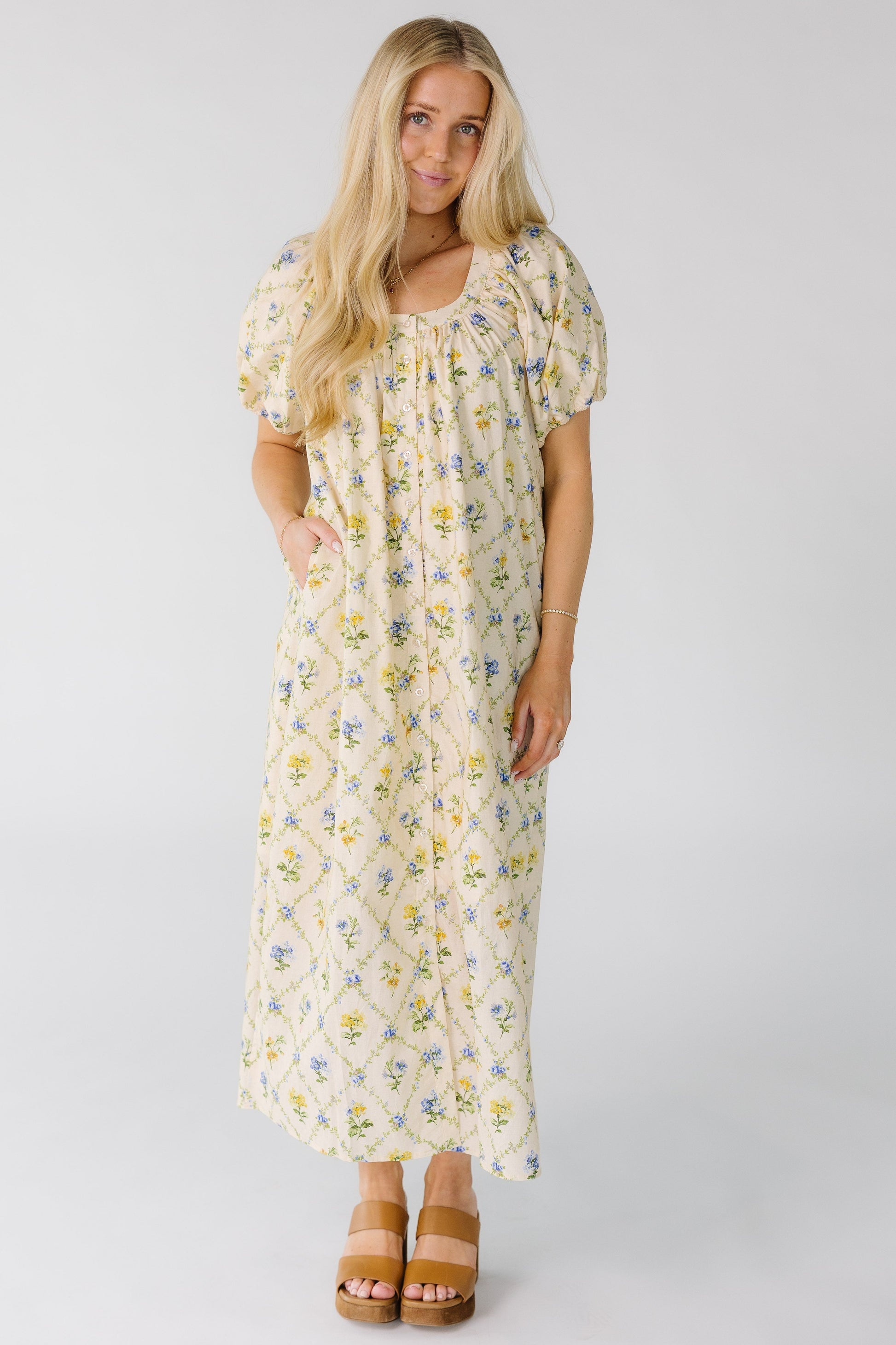 Woman wearing a loose fitting, button down midi dress in cream floral print with side pockets.