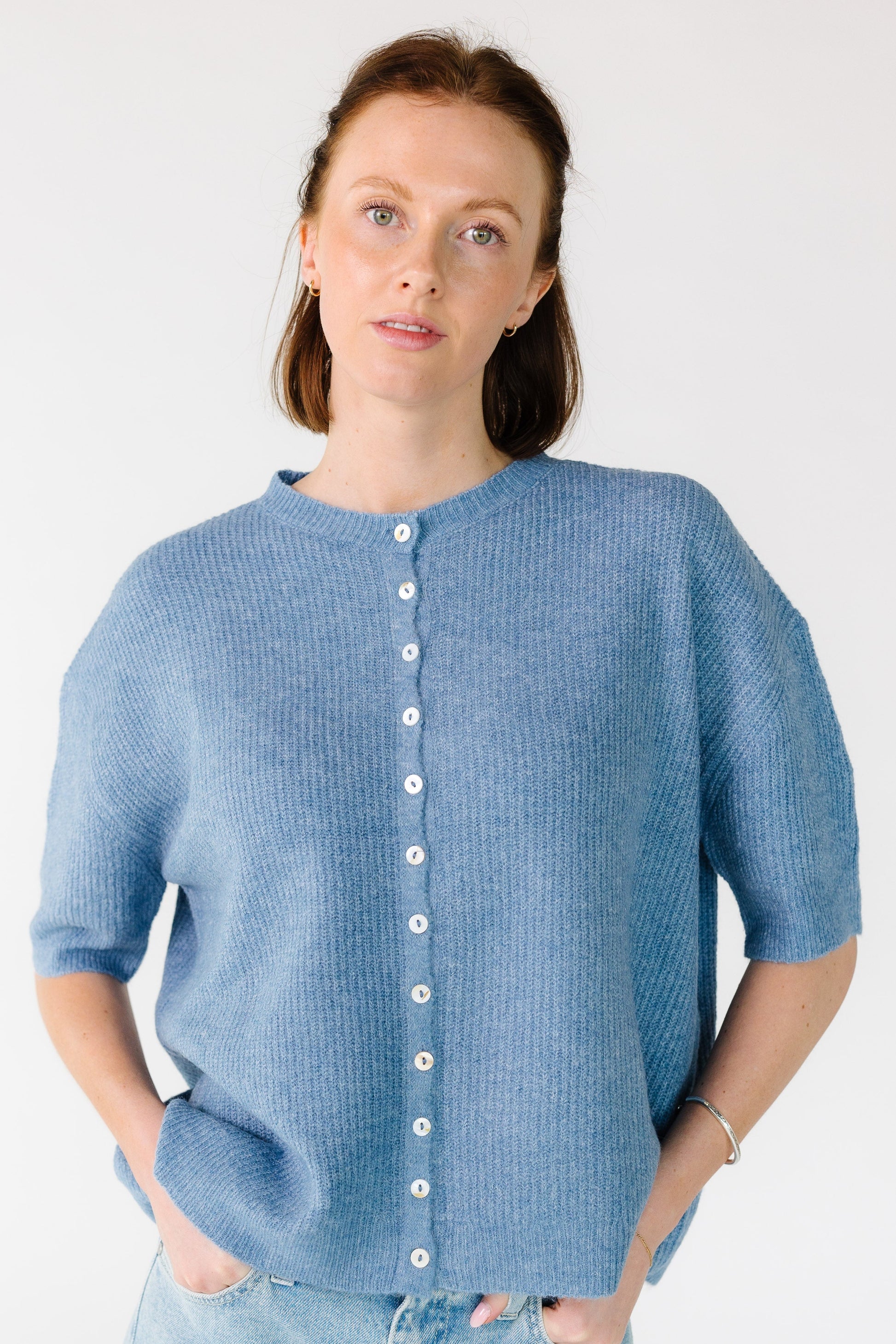 Young woman wearing a loose fitting cardigan in dusty blue with short sleeves.