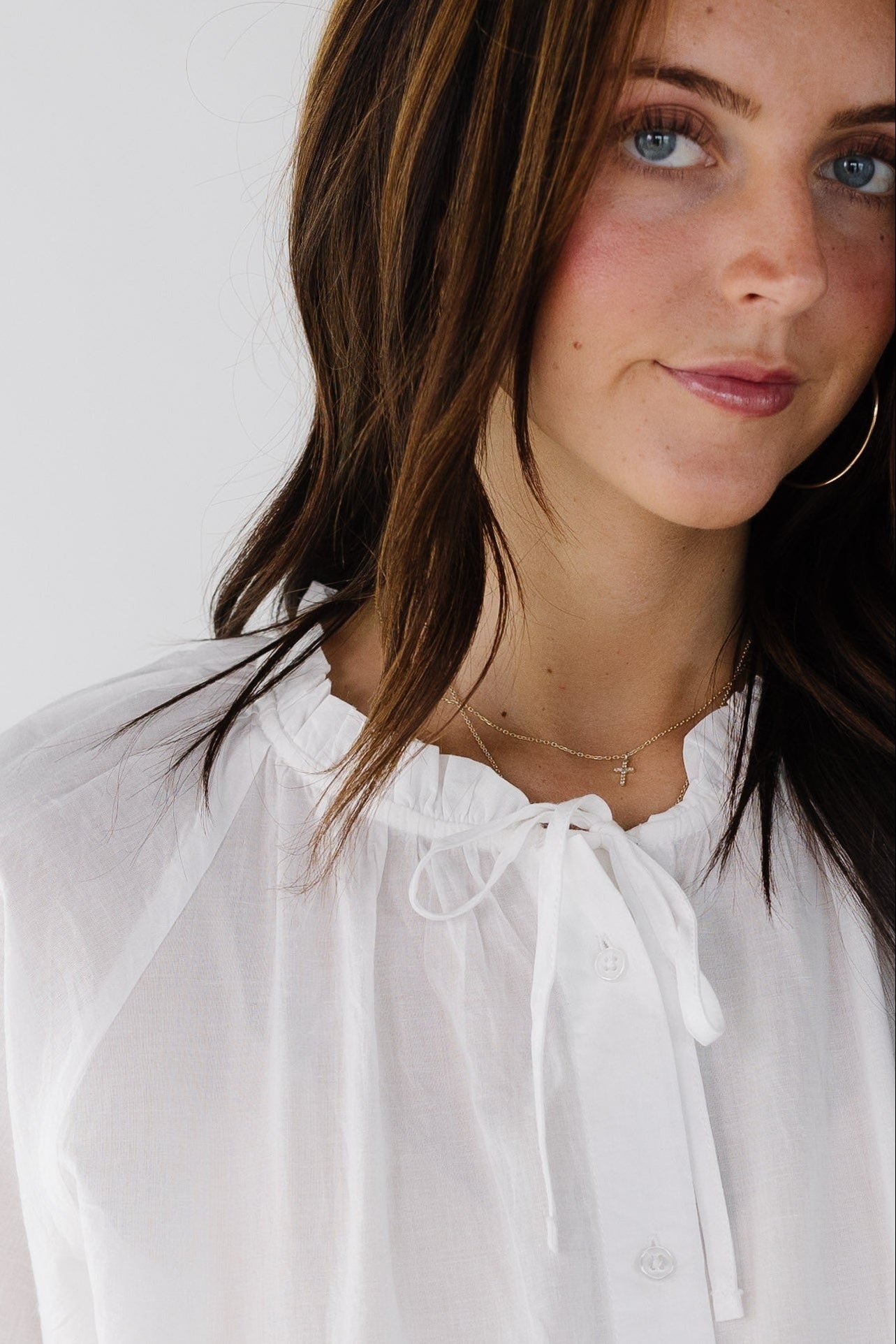 Woman wearing a loose fitting button down top with puff sleeve and a tie & ruffle neckline.