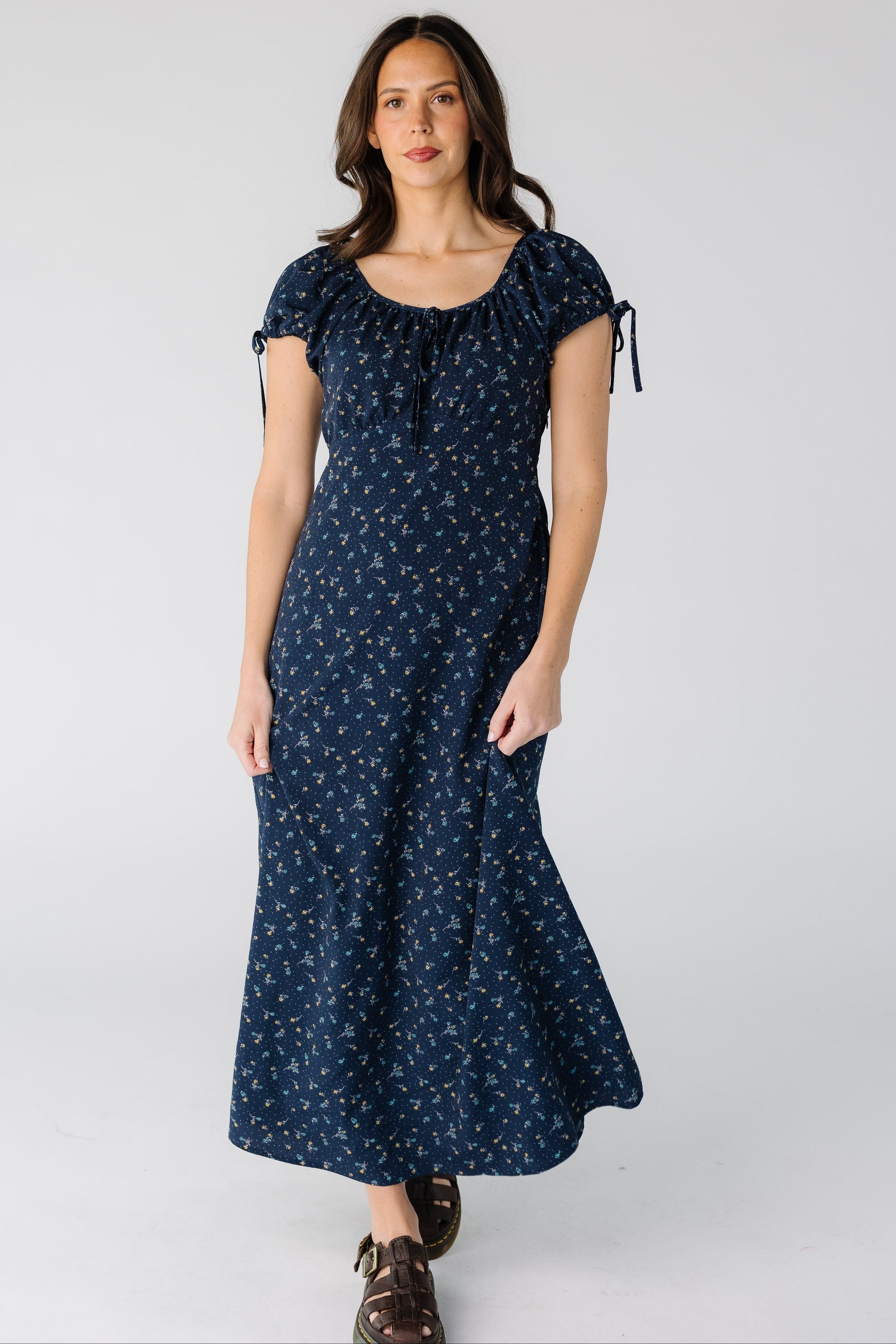 Woman wearing a modest navy floral midi dress with a square neckline and short puff sleeve and a pointed empire waist.