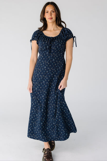 Woman wearing a modest navy floral midi dress with a square neckline and short puff sleeve and a pointed empire waist.