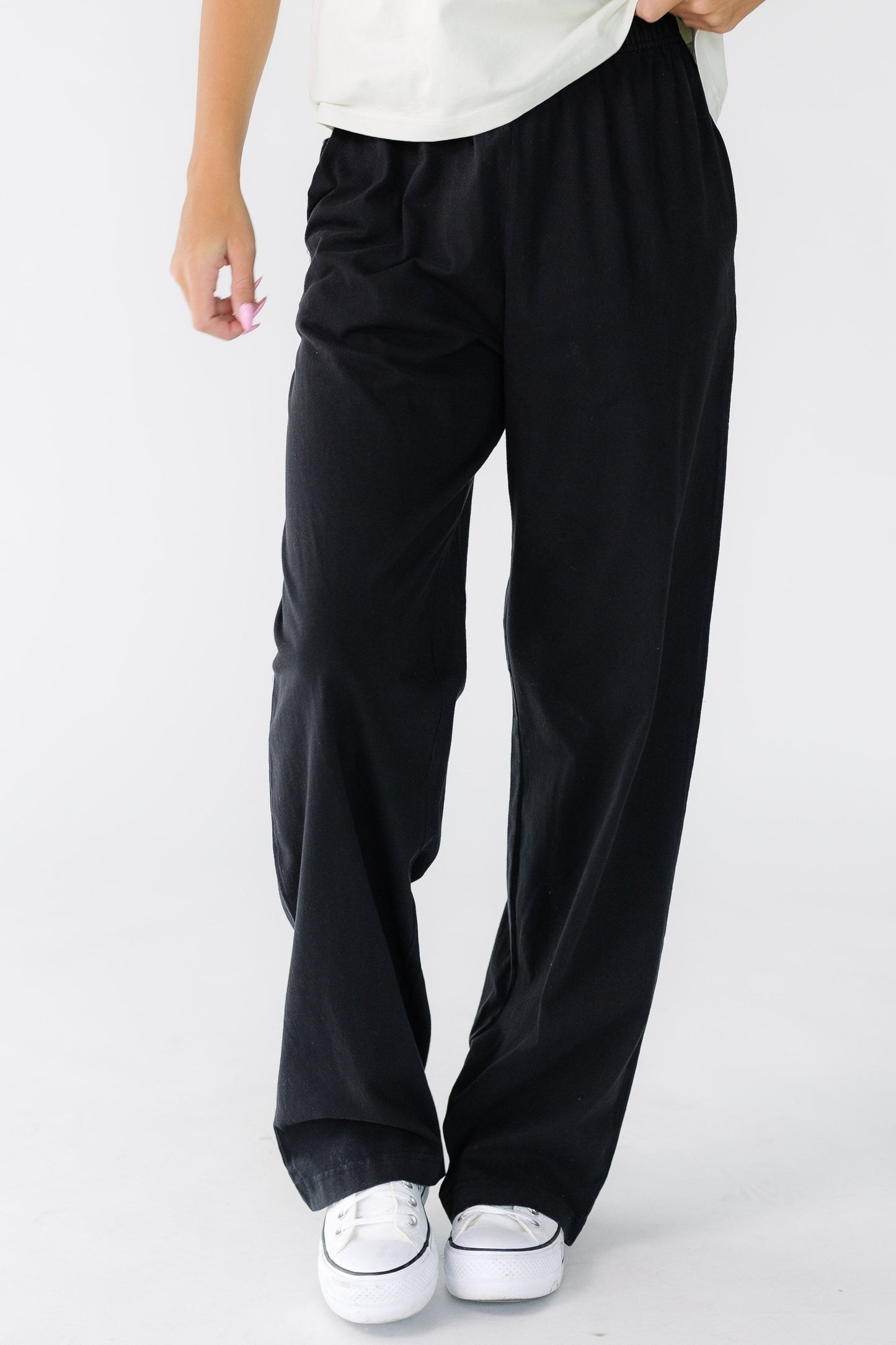 Woman wearing a pair of black, loose fitting pants with wide elastic waist and side pockets.