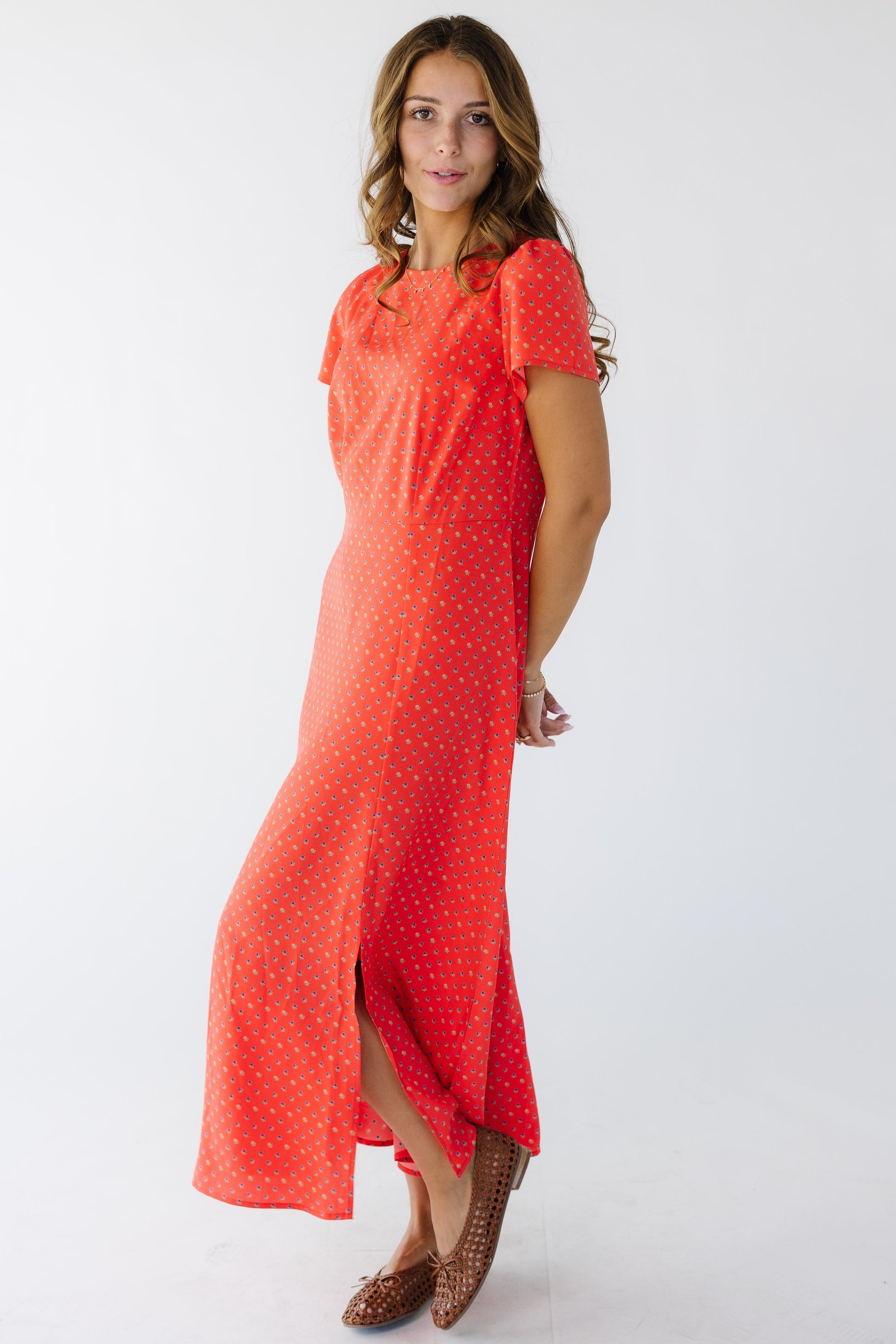 Young woman wearing a red floral midi sheath dress with short sleeves and an off center front slit.