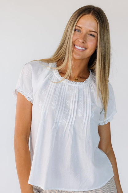 Young woman wearing a modest white short sleeve blouse with a round lace trimmed neckline and embroidery, lace and pleat details.