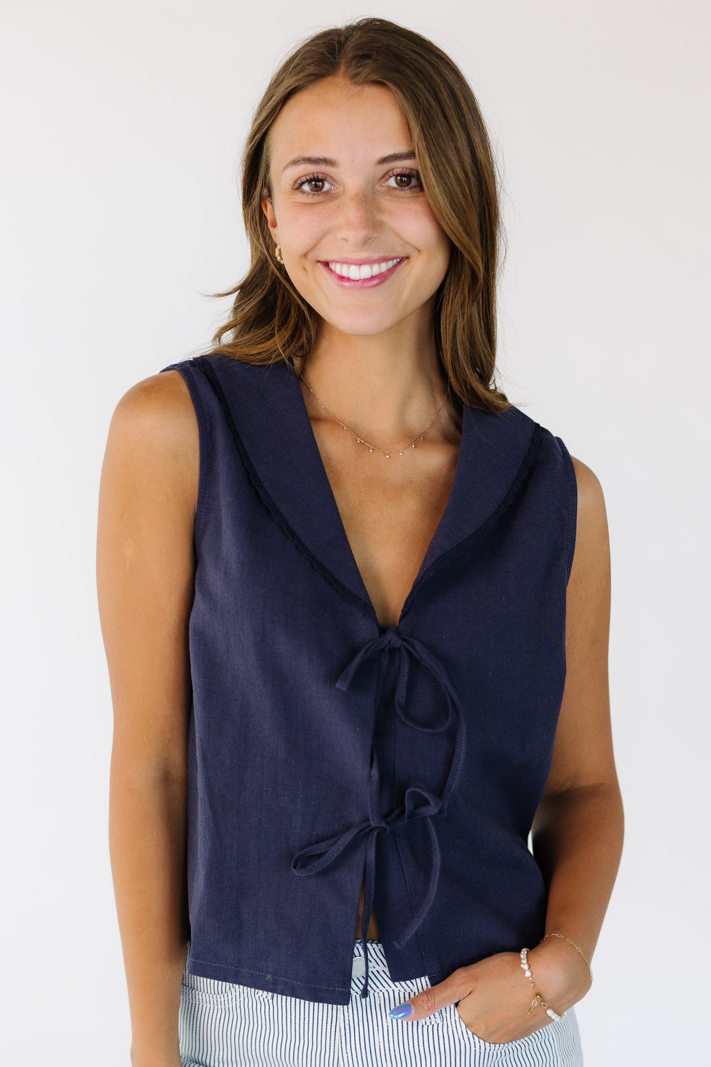 Woman wearing a loose  fitting navy sleeveless top, with a lace edge shawl collar and a 2 front tie closure.