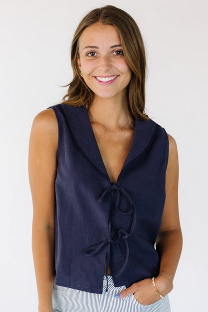 Woman wearing a loose  fitting navy sleeveless top, with a lace edge shawl collar and a 2 front tie closure.