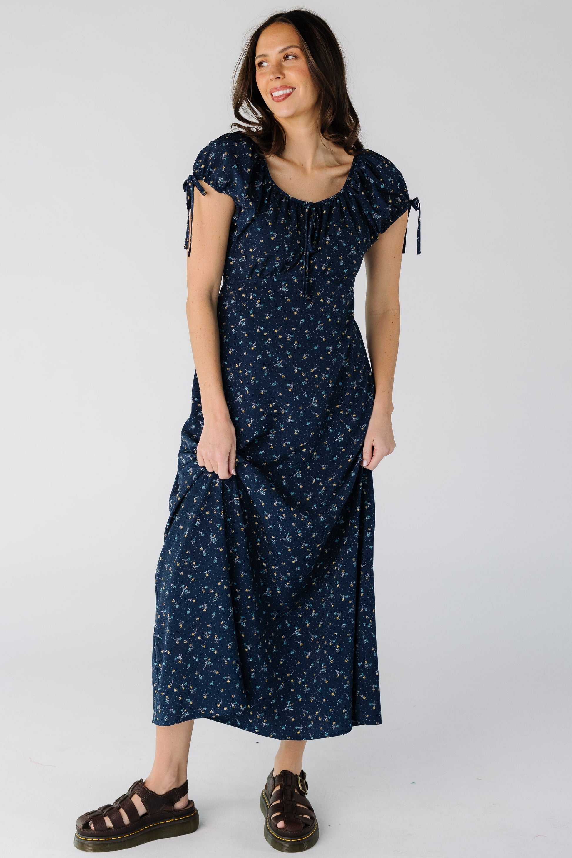 Woman wearing a navy floral midi dress with a pointed empire waist and short puff sleeves.