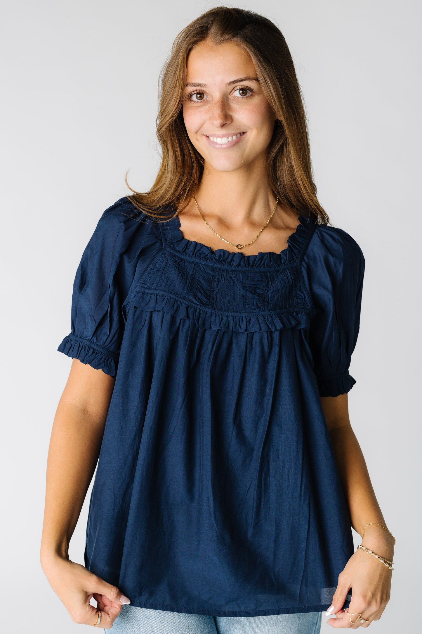 Woman wearing a navy loose fitting blouse with a pleated and ruched  yoke and short sleeves