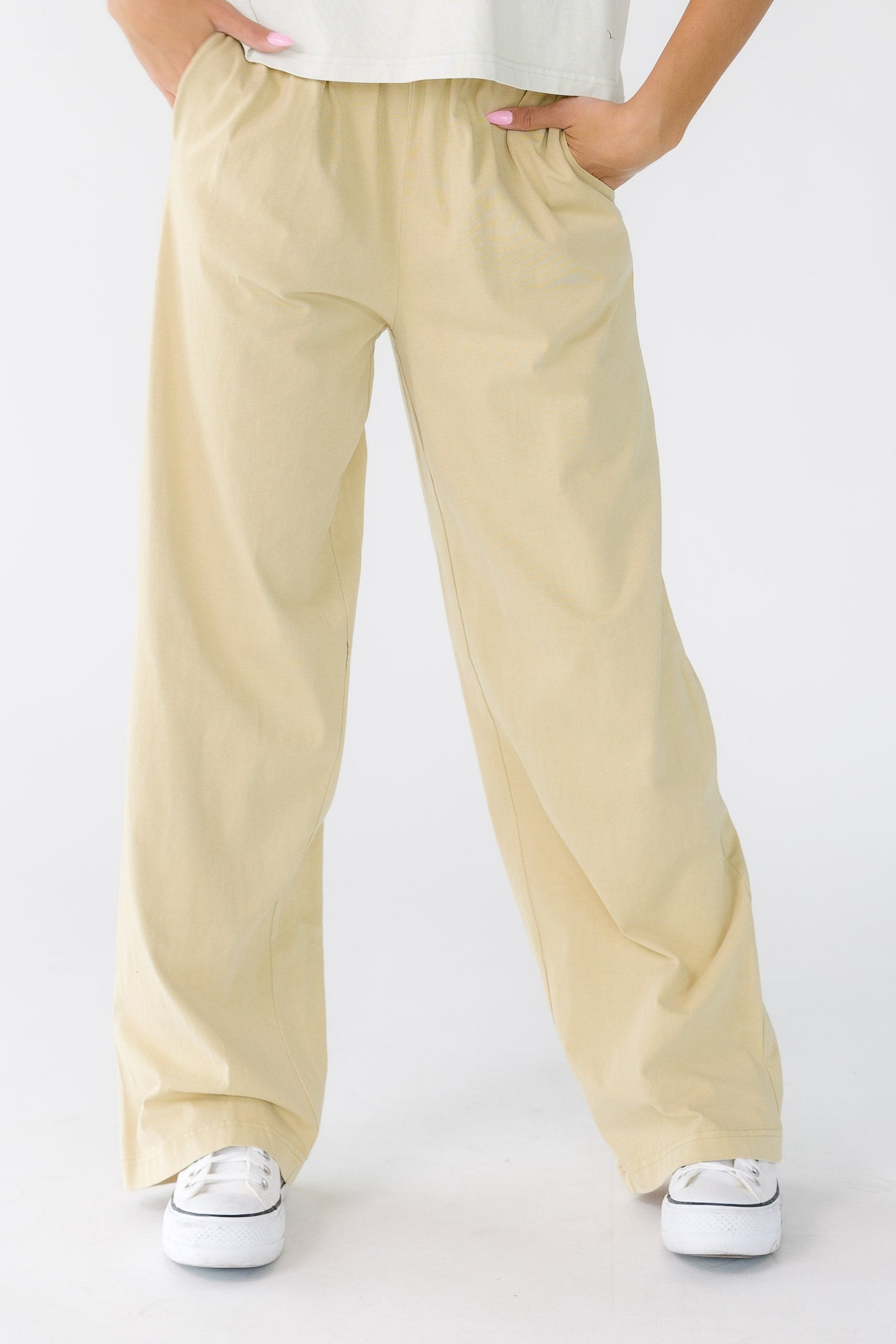 Young woman wearing a pair of light beige wide leg pants with side pockets.