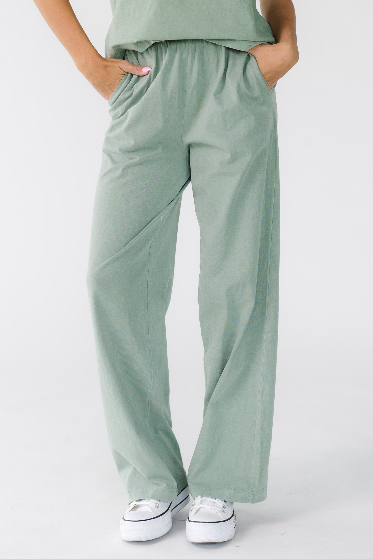 Woman wearing a pair of modest sage green loose fitting pants with a wide elastic waistband and side pockets.