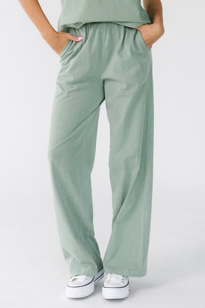 Woman wearing a pair of modest sage green loose fitting pants with a wide elastic waistband and side pockets.