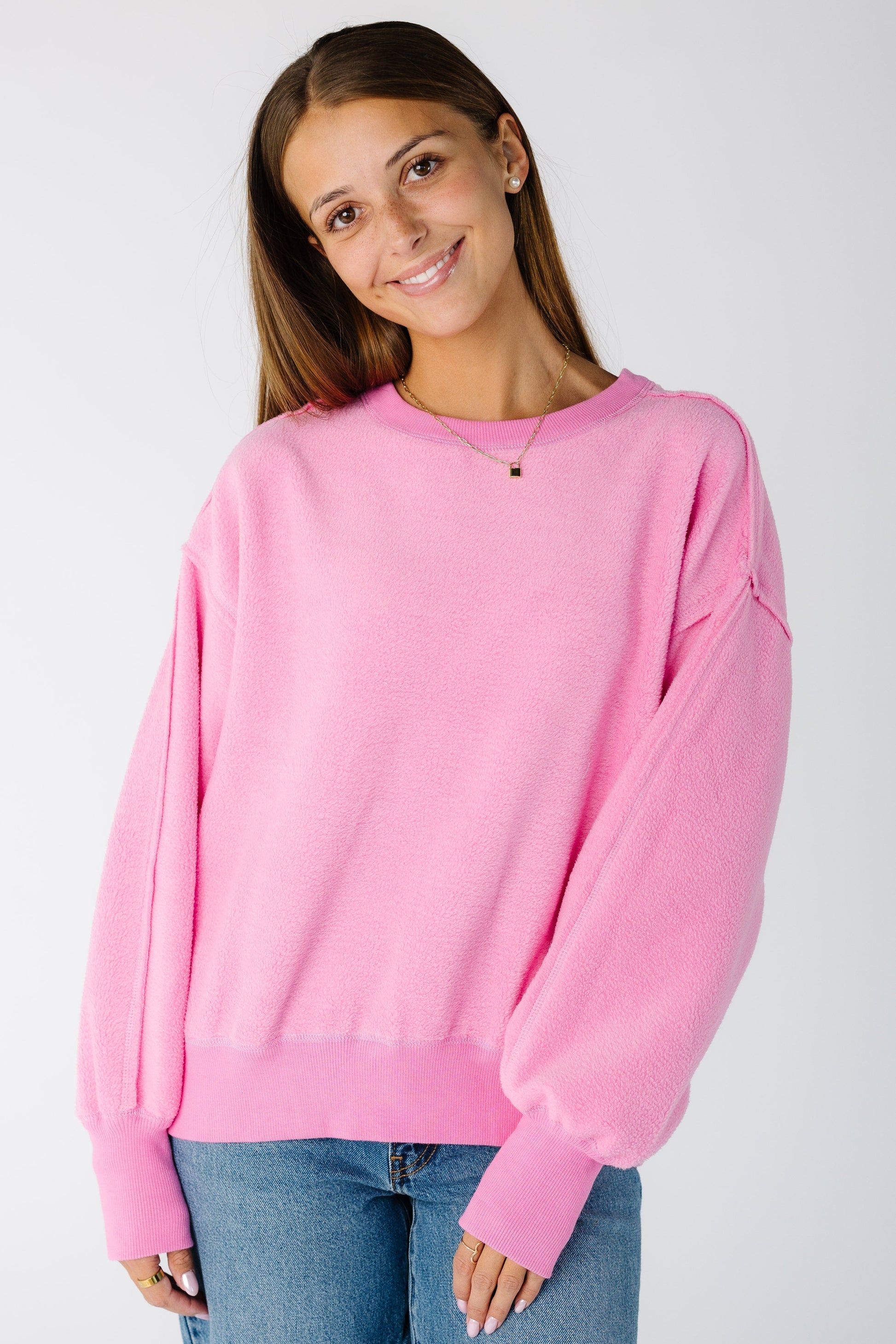 Woman wearing a loose fitting pink sweatshirt with exposed seams