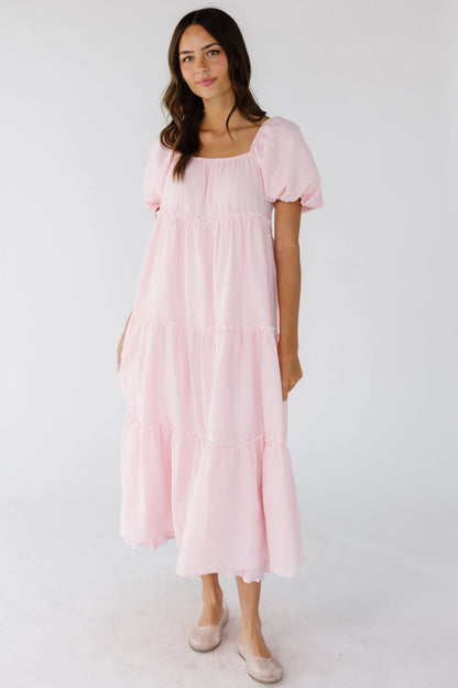 Woman wearing a loose fitting pink gingham tiered midi dress with an elastic square neckline and balloon sleeves.