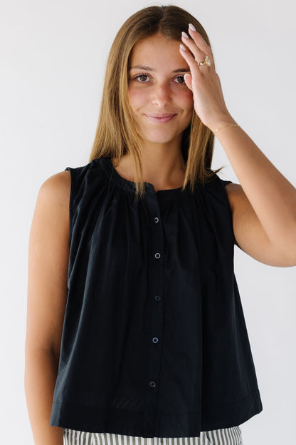 Woman wearing a sleeveless black button down top that is loose fitting.