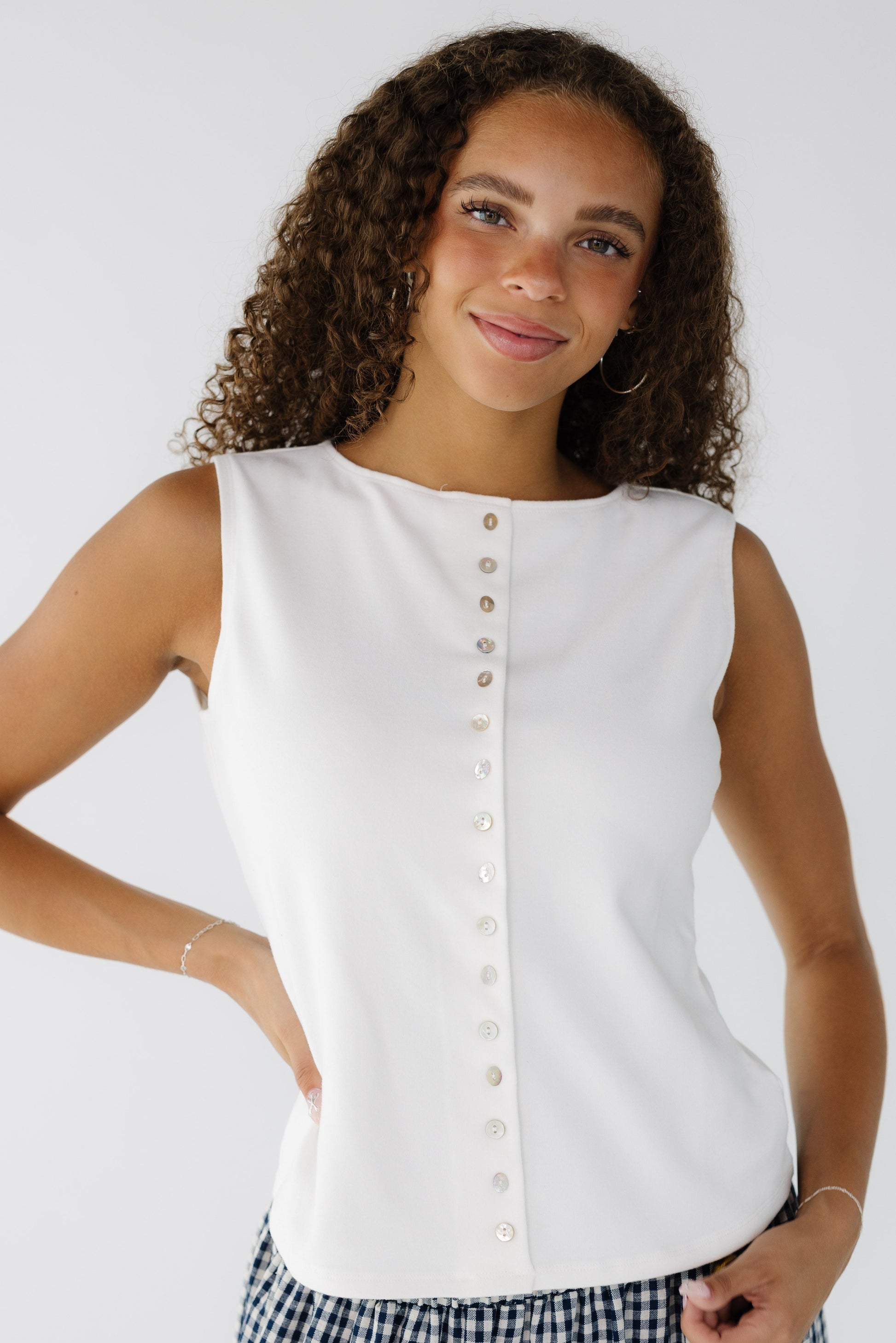 Teenage girl wearing a white sleeveless top with a high round neckline and functioning front shell buttons.