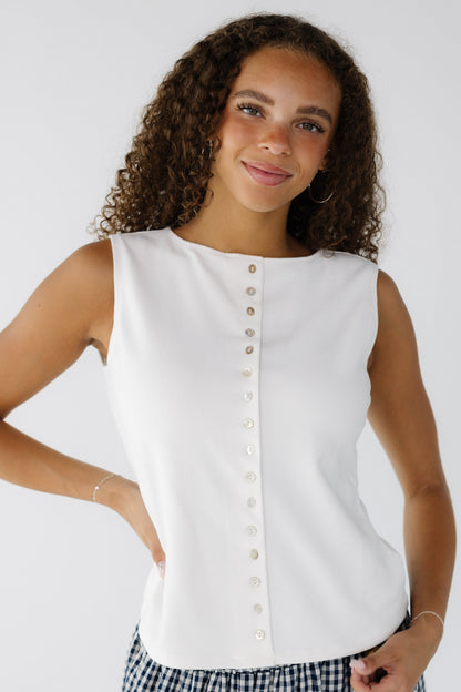 Teenage girl wearing a white sleeveless top with a high round neckline and functioning front shell buttons.