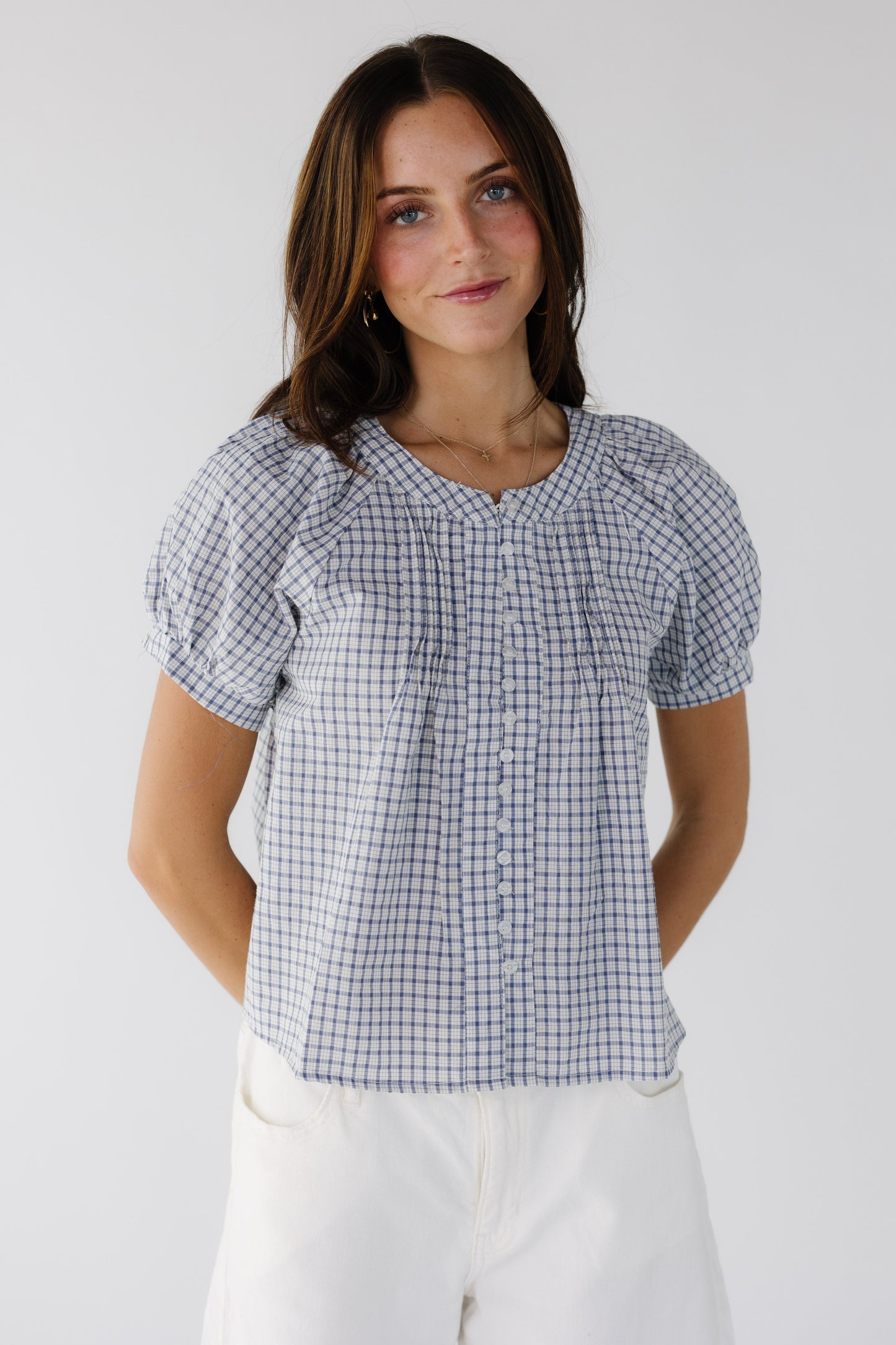 Young woman wearing a blue & white plaid button down blouse with a round neckline and puff sleeves.