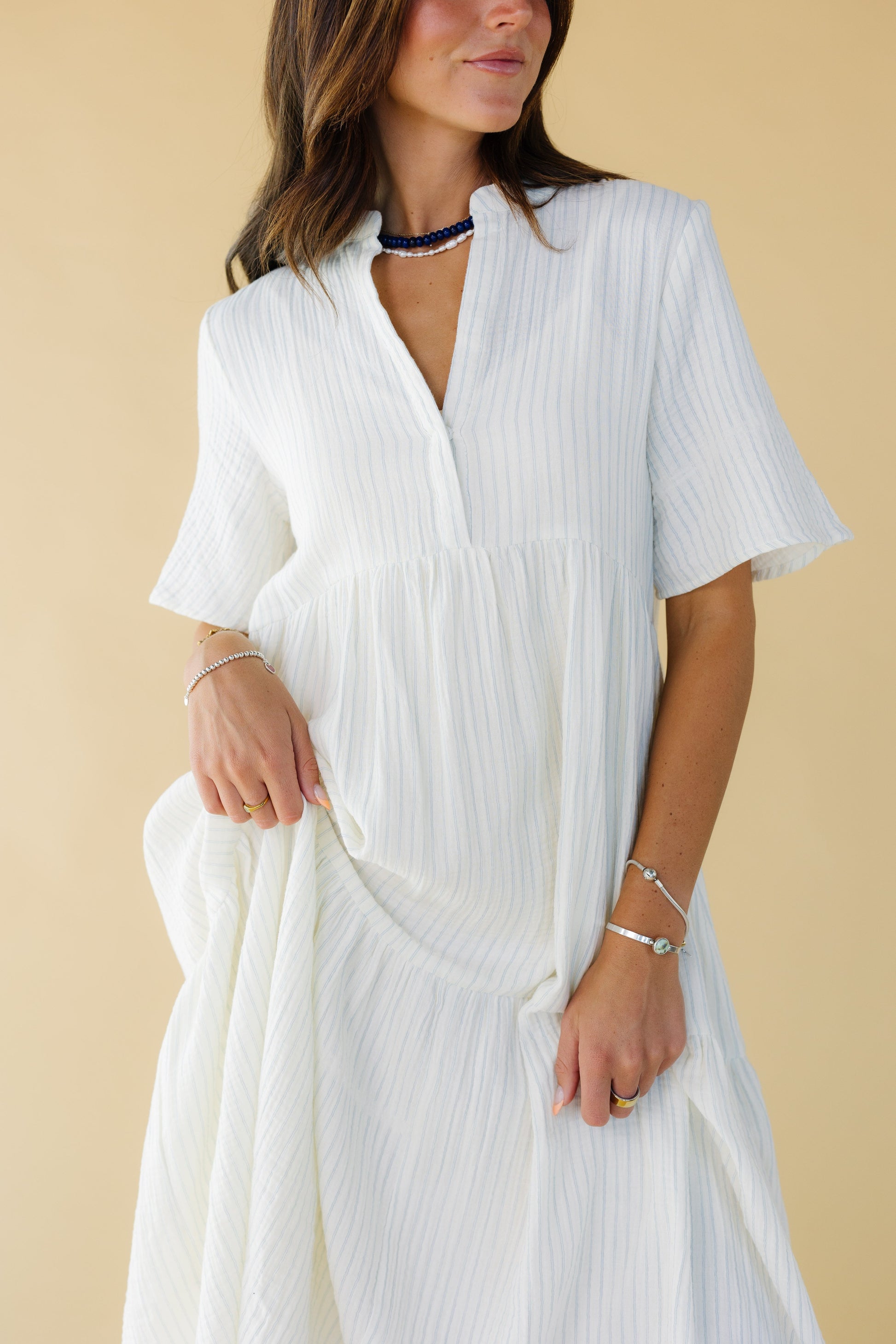Close view of a woman wearing a white and light blue stripe with a V-neckline and elbow length sleeves.