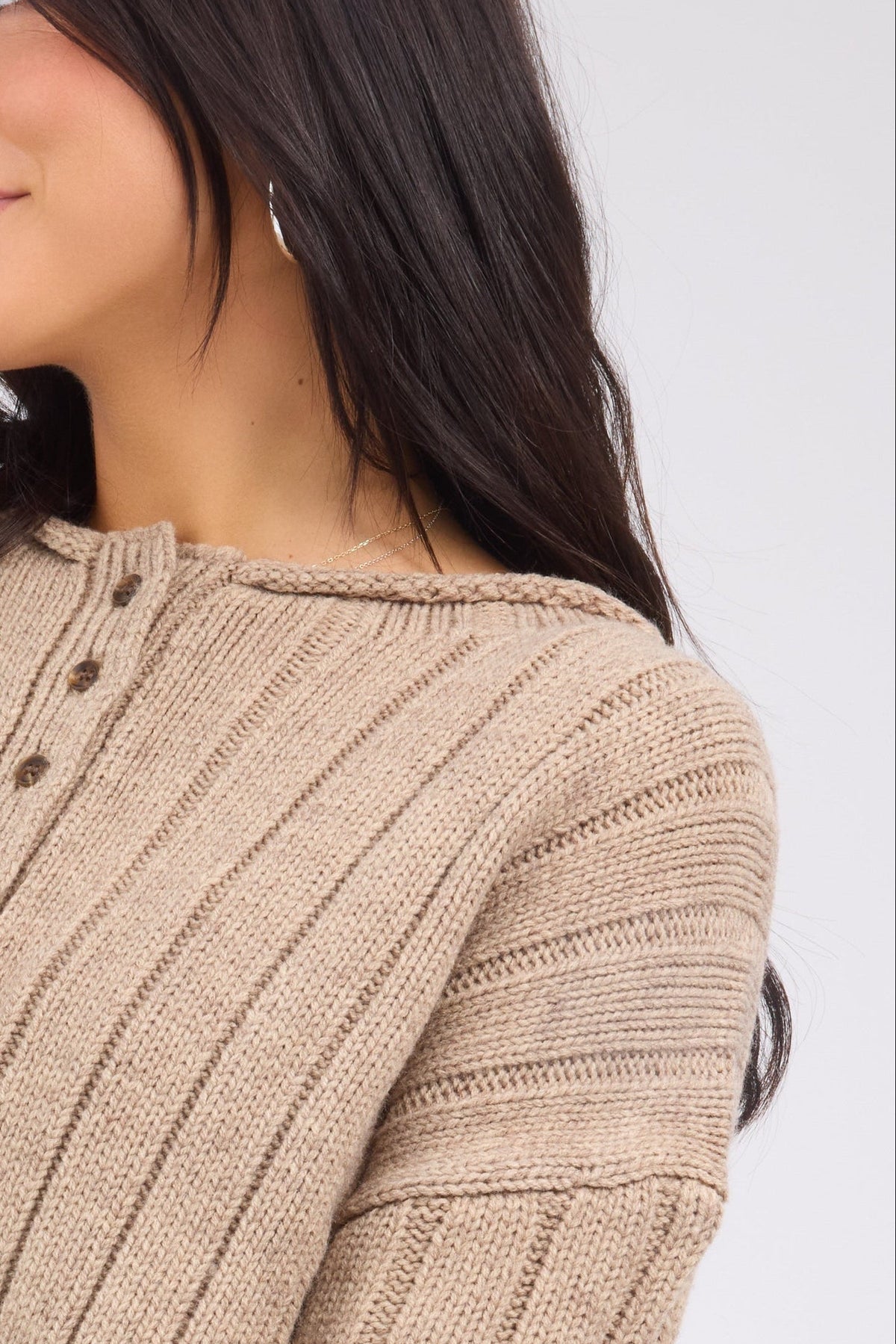A young woman wearing a wide ribbed cardigan with a rolled collar and long sleeves.