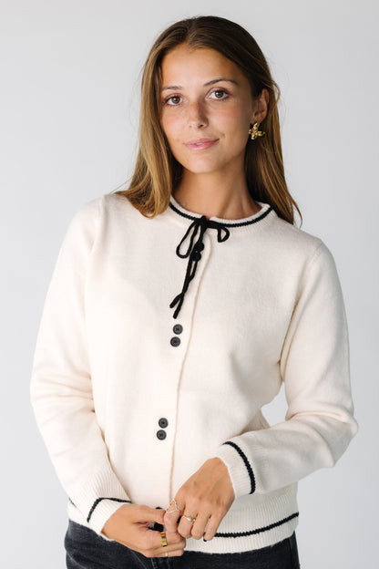 Woman wearing an ivory button down cardigan with black details