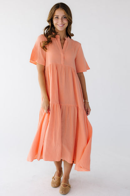 Woman wearing a coral loose fitting midi dress with a wide bottom ruffle, short sleeves and a V-neckline.