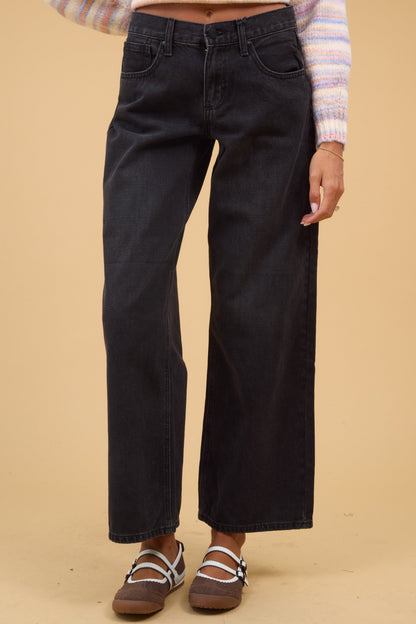 Woman wearing wide leg jeans in washed black with a zipper-button closure.
