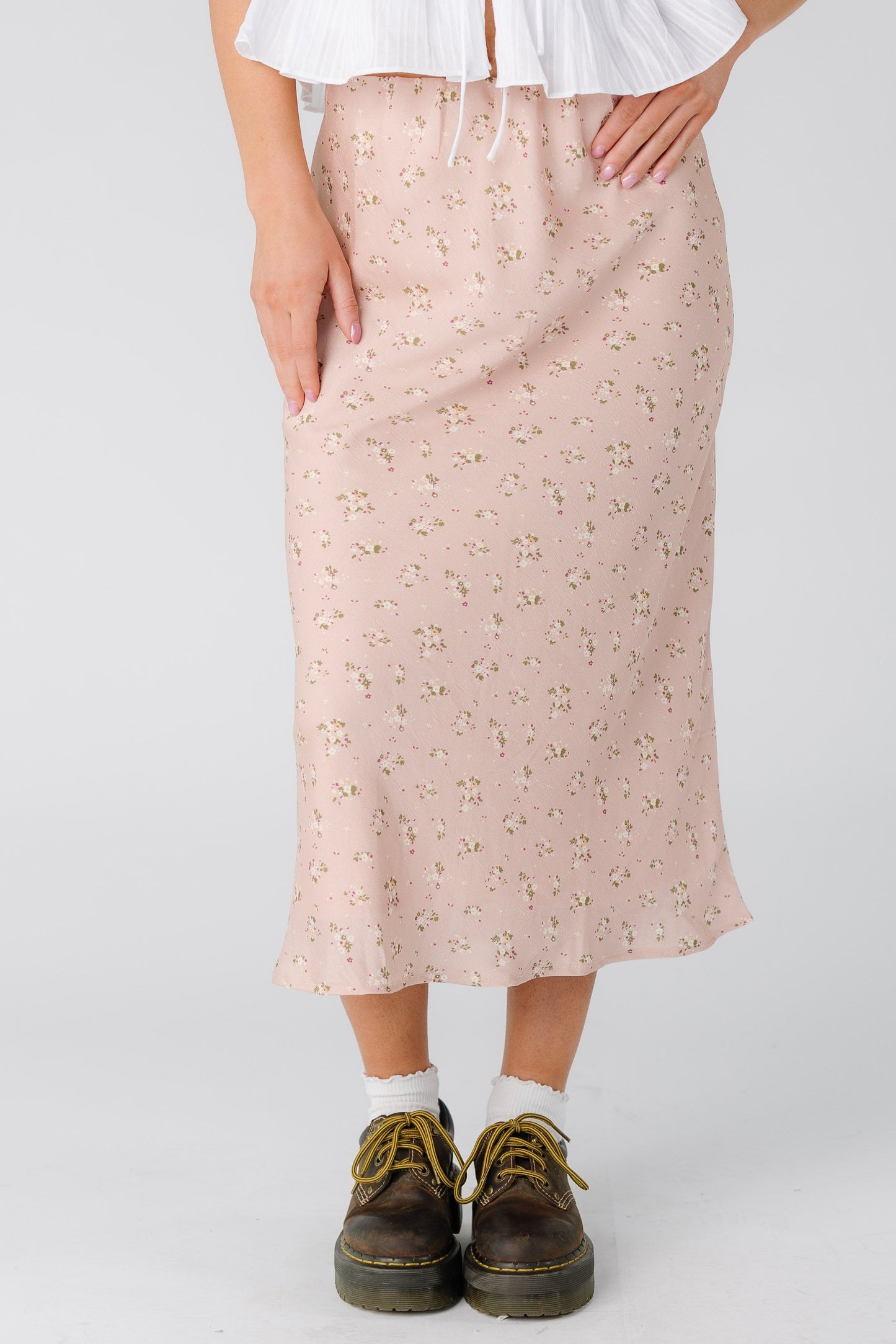 Woman wearing an A-line midi skirt in light pink with a cream floral print.