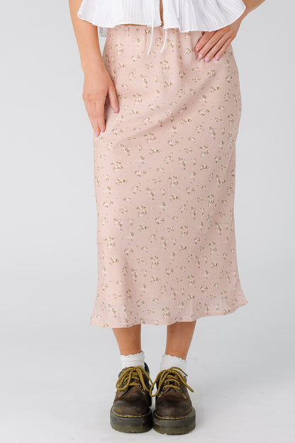 Woman wearing an A-line midi skirt in light pink with a cream floral print.